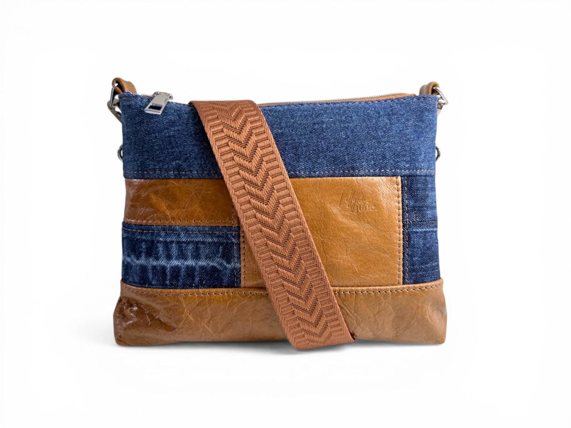 Upcycled denim and rescued tan coloured leather, patch crossbody bag, with the tan coloured woven crossbody strap wrapped around the bag, sat on a white background