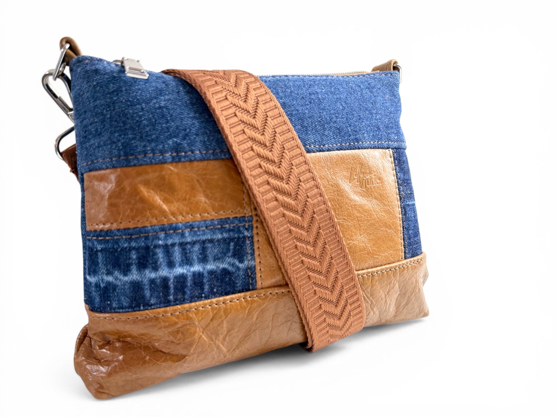 Front quarter view of the Bonny crossbody bag; a blue denim and tan brown leather patchwork bag with a strap on a white background