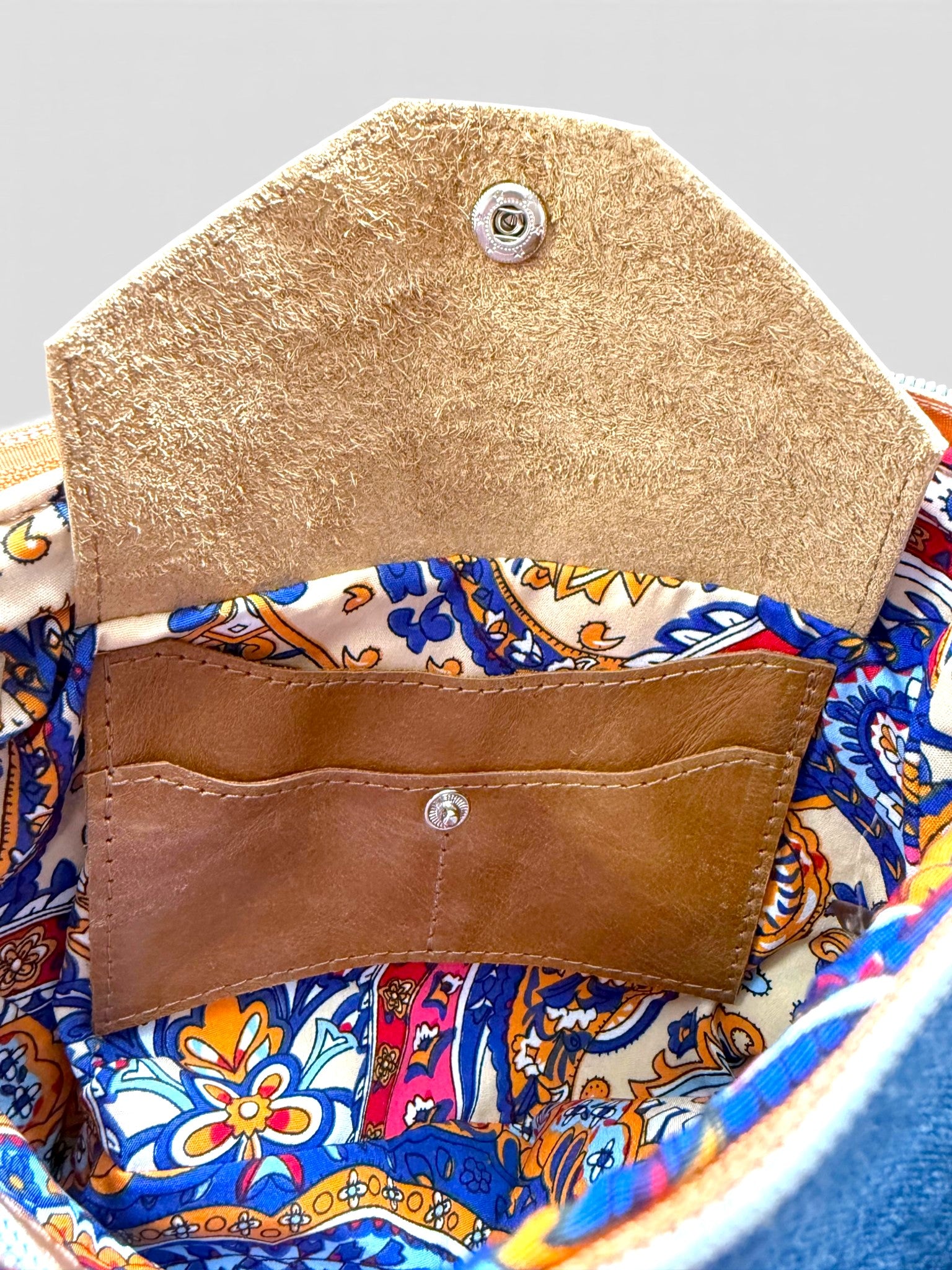 Close-up of a colorful fabric interior with a tan leather integrated pocket with the studded flap open
