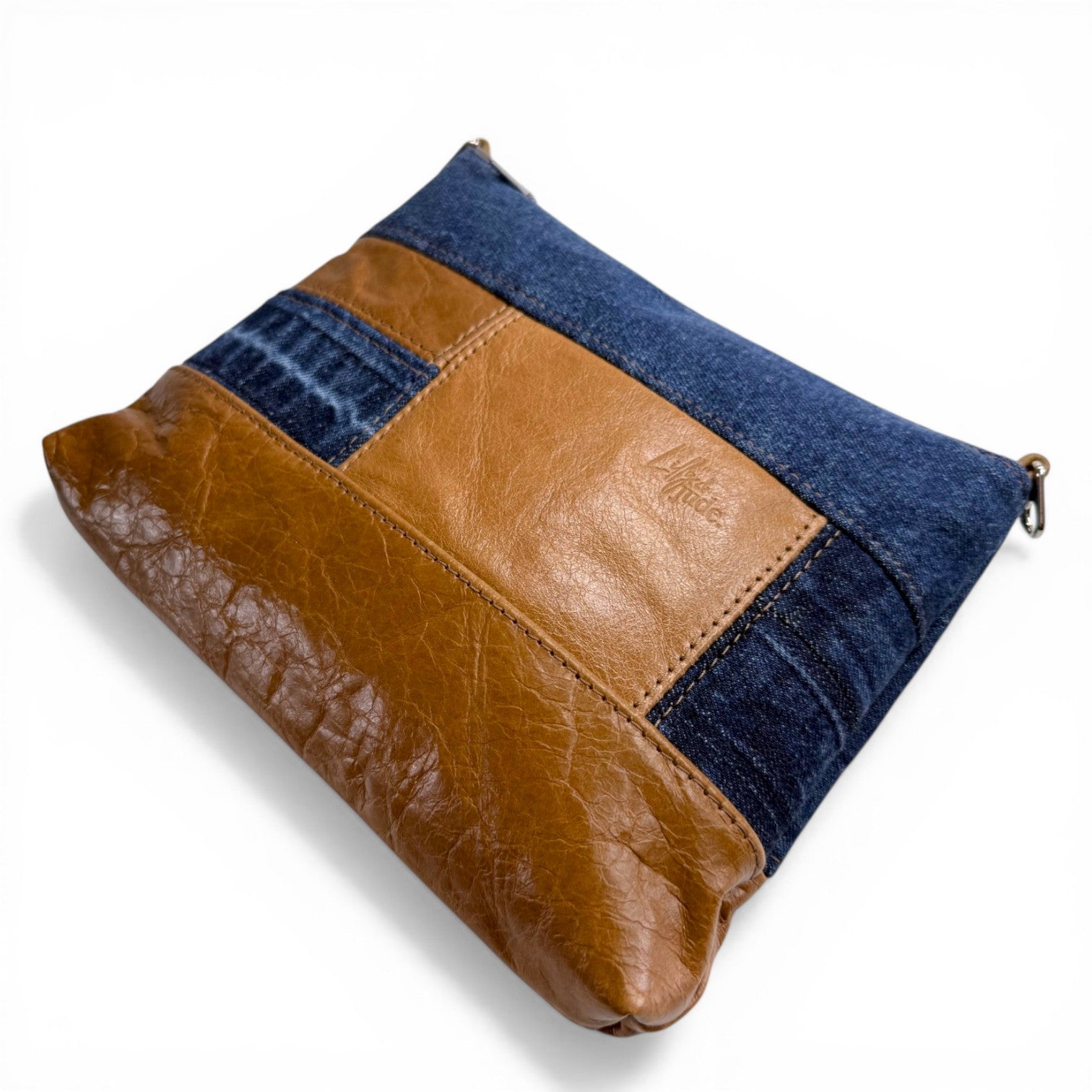 Patchwork crossbody bag with tan brown leather and blue denim sections lying on a white background
