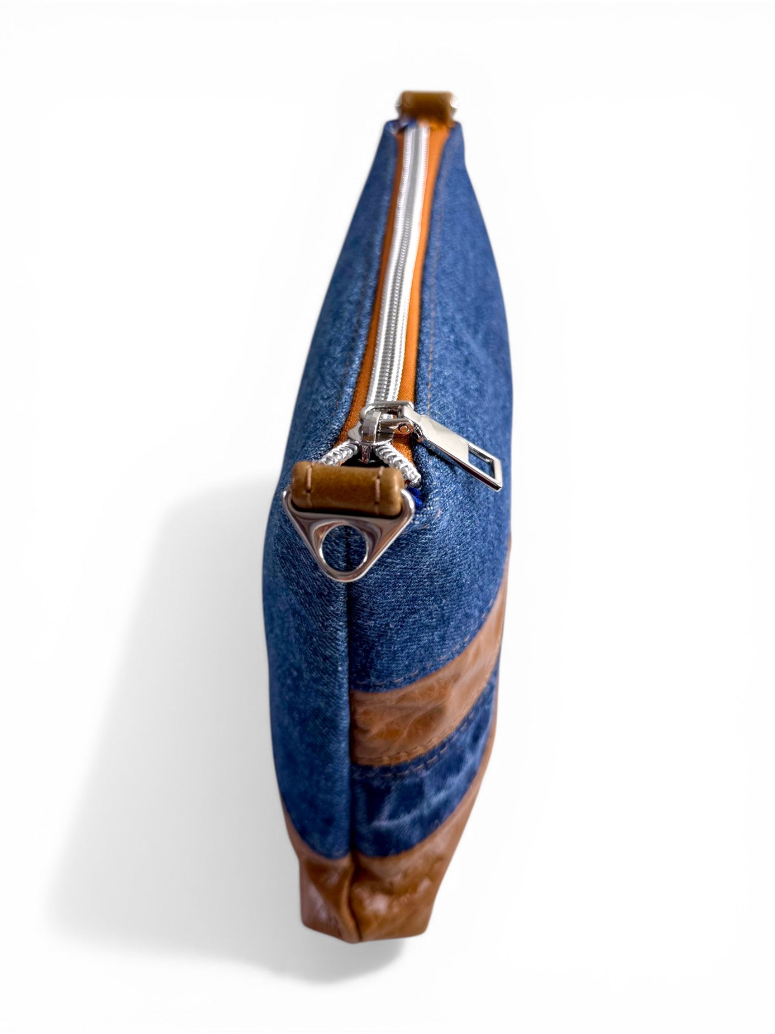 View from above of a denim and tan leather cross body bag, with a silver zipper and hardware on a white background