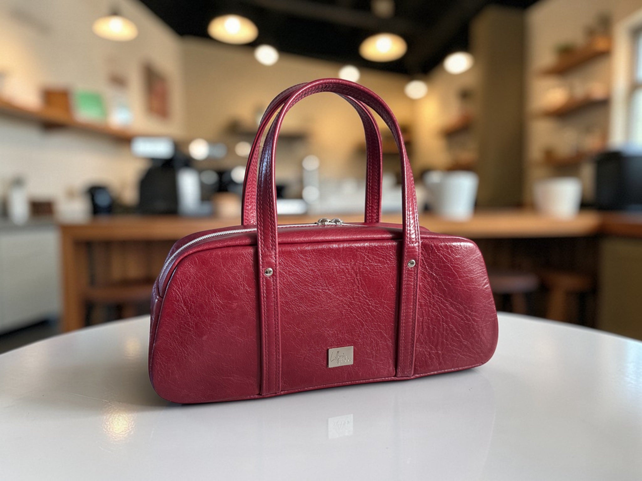 Burgundy red leather handbag on a white surface with a blurred background of a cafe.