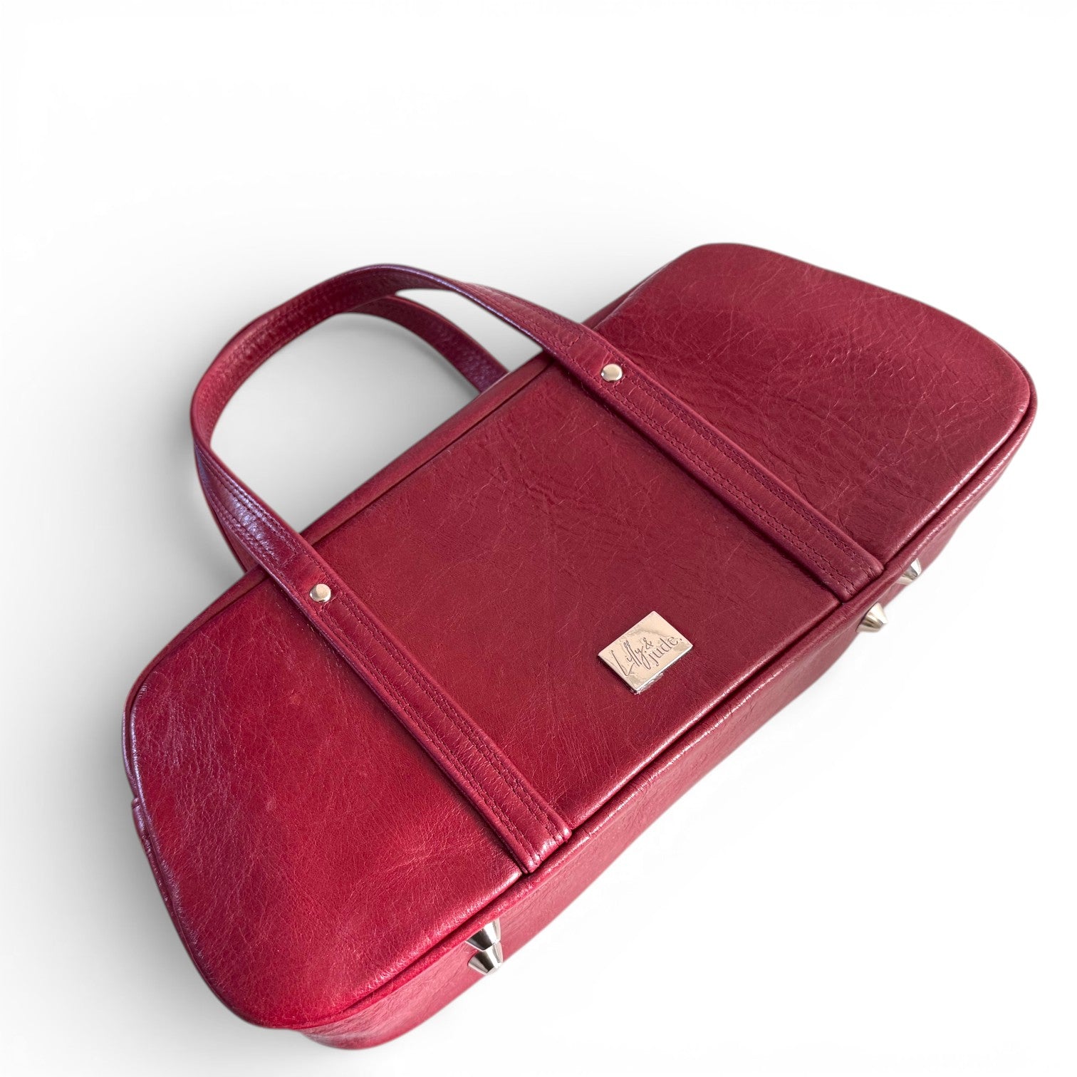 Red leather handbag with a visible Lilly & Jude brand logo lying on a white background