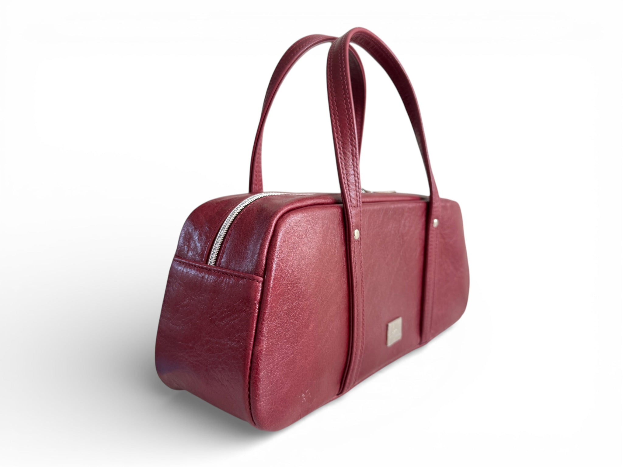 Side quarter view of the dark red leather handbag on a white background