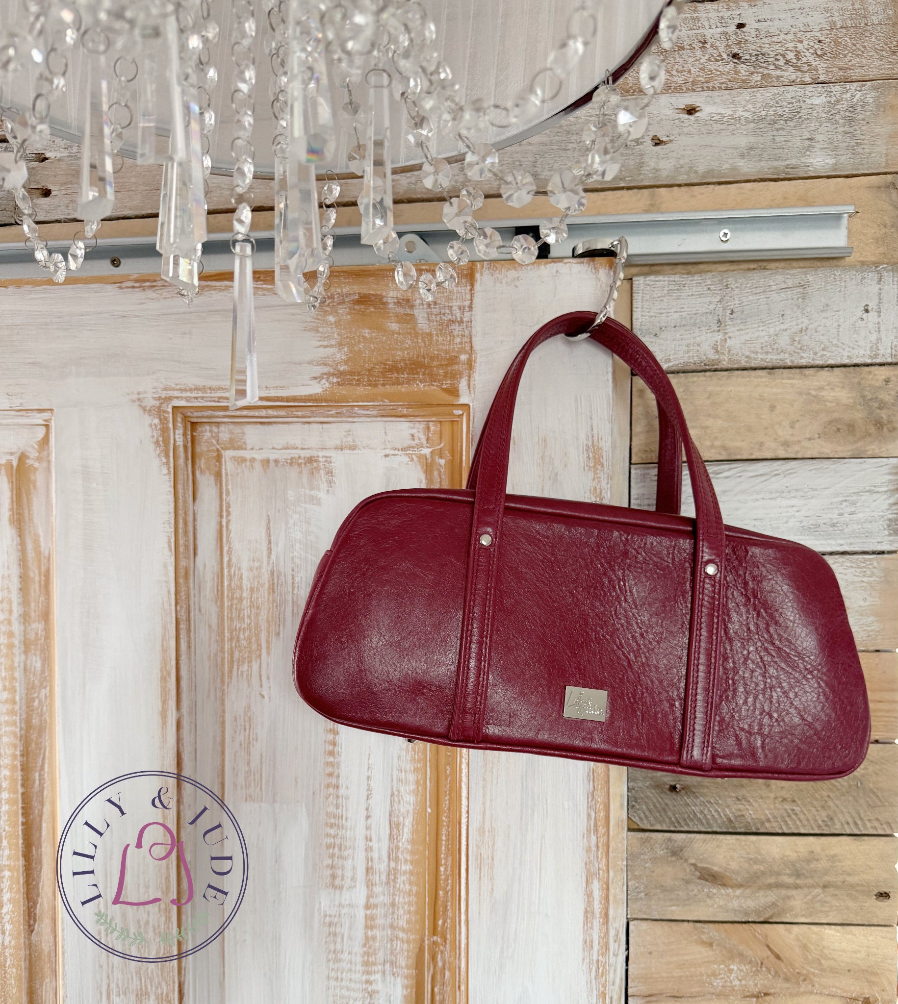 Red leather handbag hanging from a chandelier against a wooden wall.
