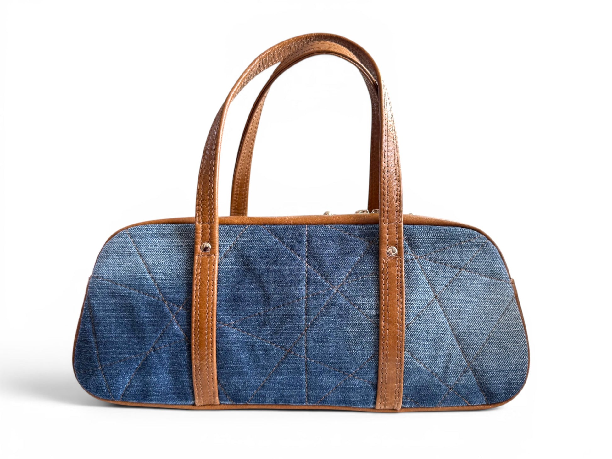View of the back of the Cassie, an elongated bowling style bag, made from upcycled denim jeans, with tan coloured leather shoulder strap. The image highlights the geometric stitched quilting, on a white background