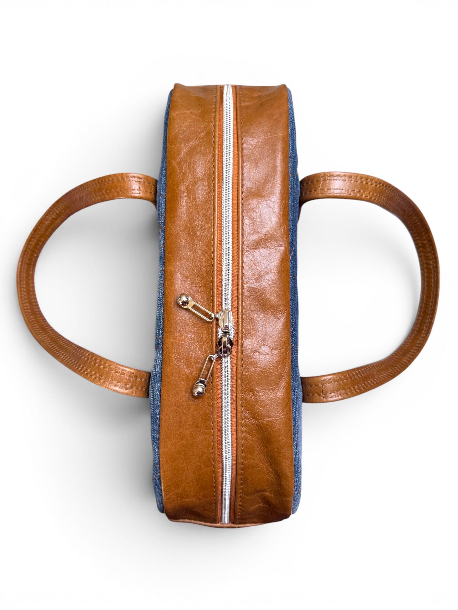 Birds eye view of the top of the Cassie baguette bag, highlighting the closed silver zipper and straps