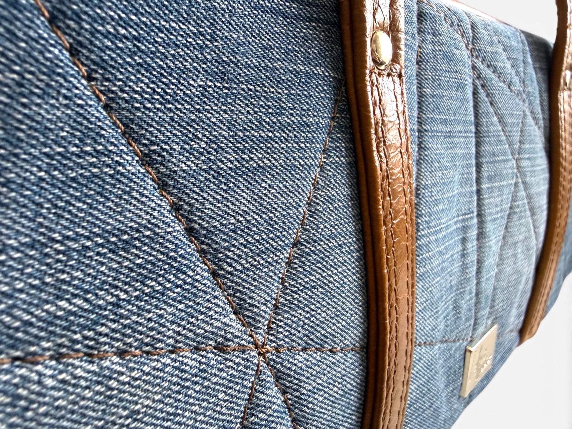 Close-up of a blue denim bag with brown leather trim and stitching detail.