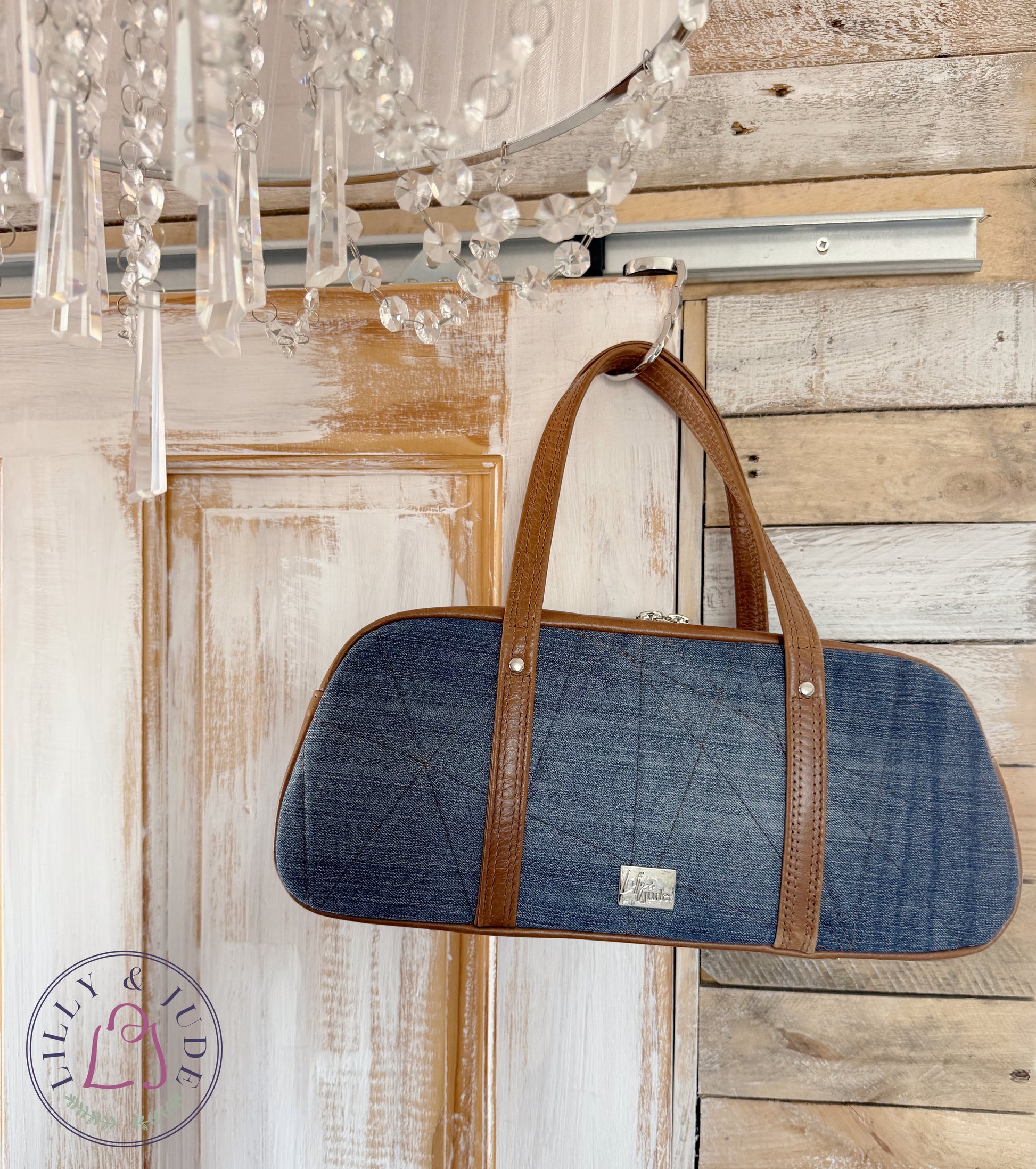 Cassie denim and leather handbag, hanging from the corner of a rustic looking door, with the Lilly & Jude logo visible