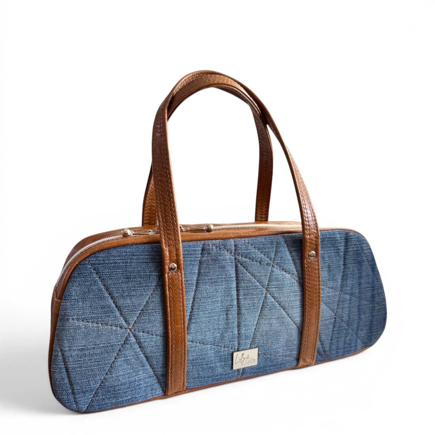 Blue denim quilted handbag with tan brown leather handles on a white background