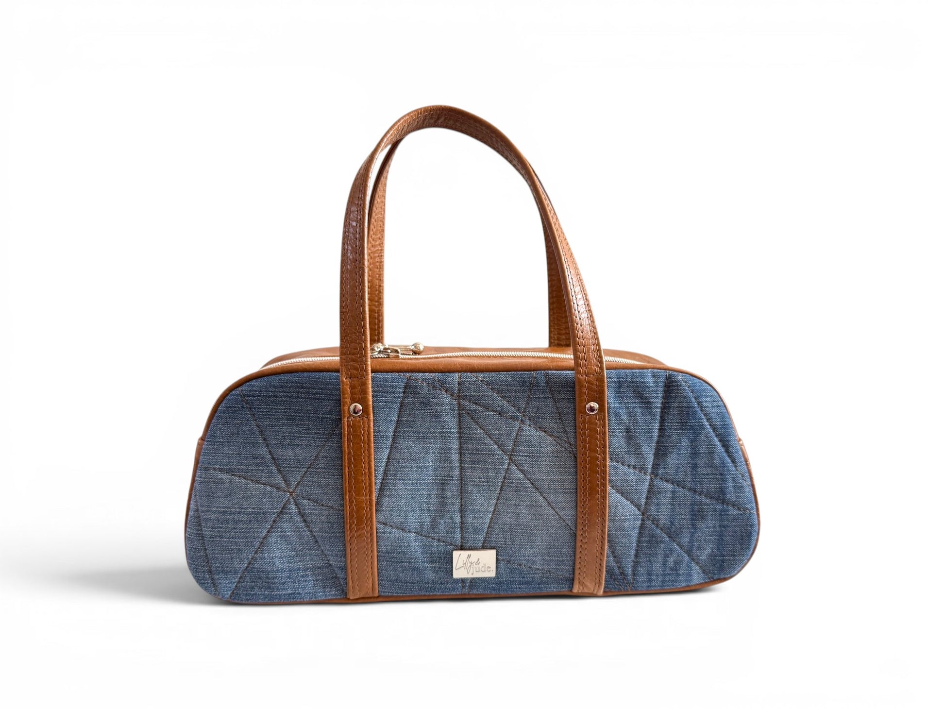 An east/west, baguette style bowling handbag, made from upcycled jeans and genuine rescued leather, sat on a white background