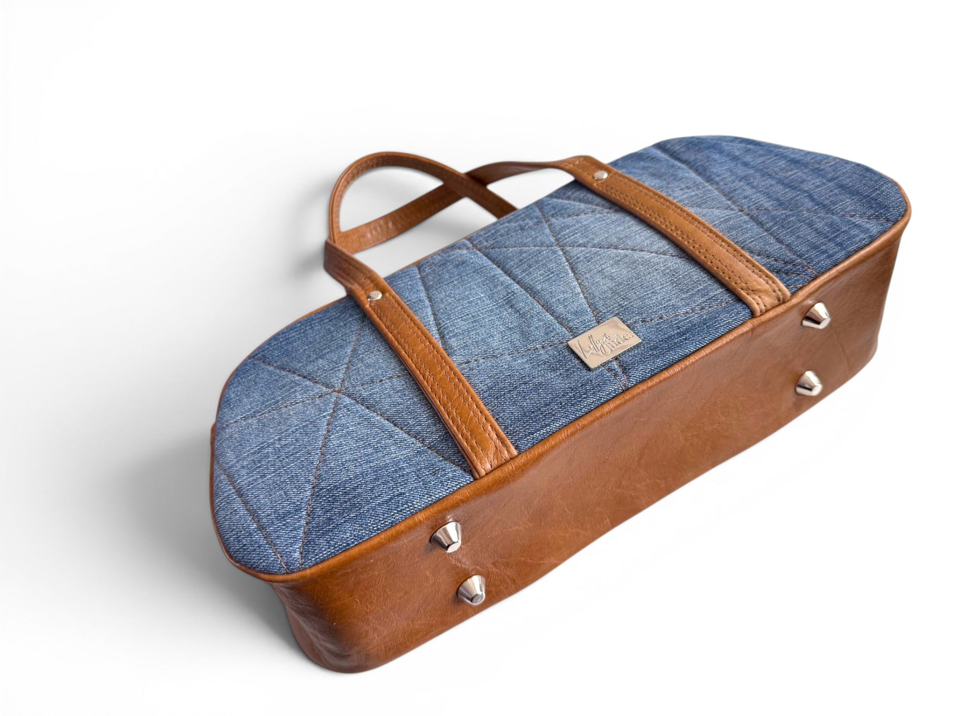 The Cassie bowling style handbag, lying down on a white background to show the bottom of the bag, which has 4 silver bag feet