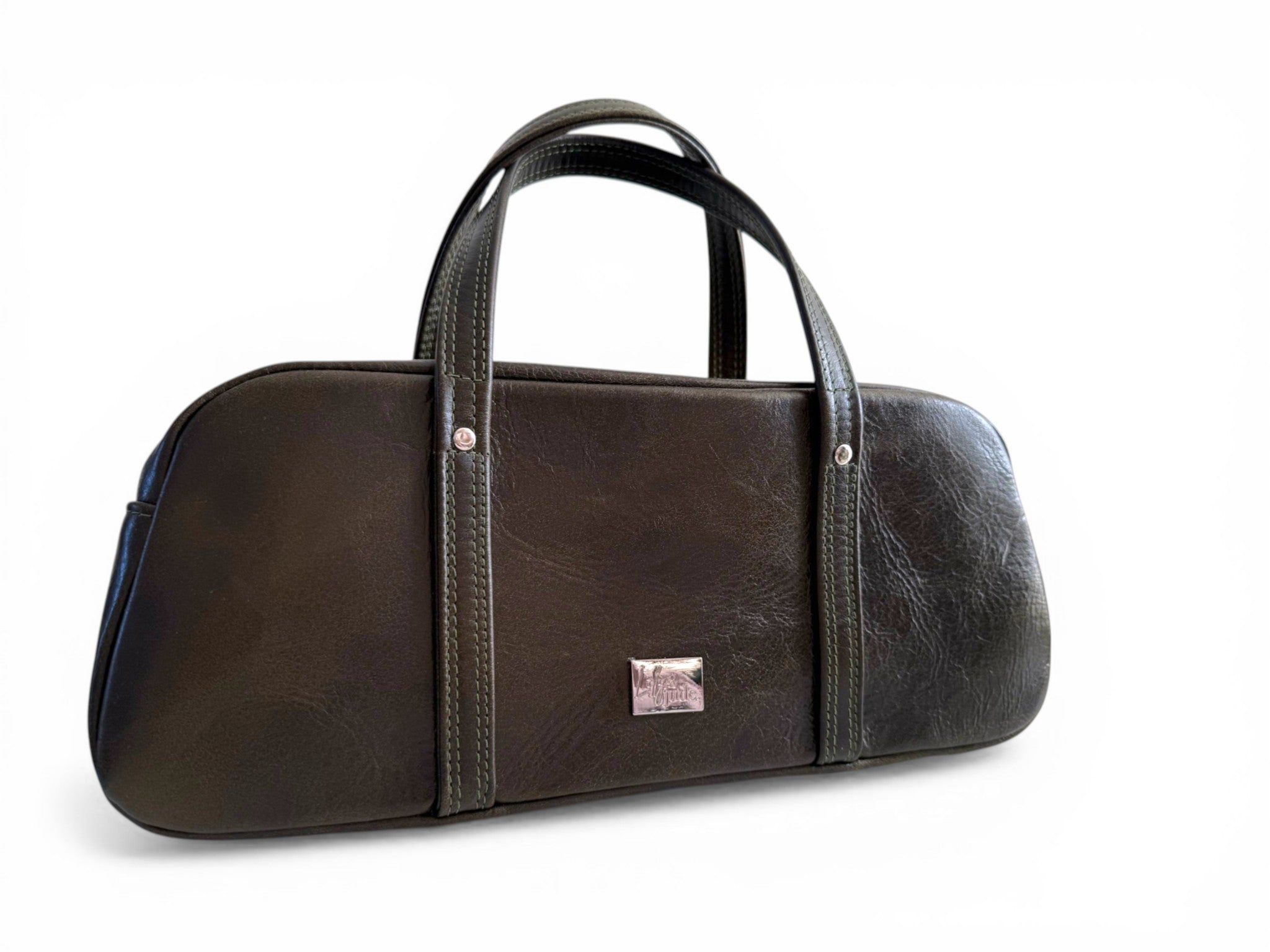 Front quarter view of a dark green leather handbag, showing the simplicity of the design, and the Lilly & Jude silver bag tag, sat on a white background
