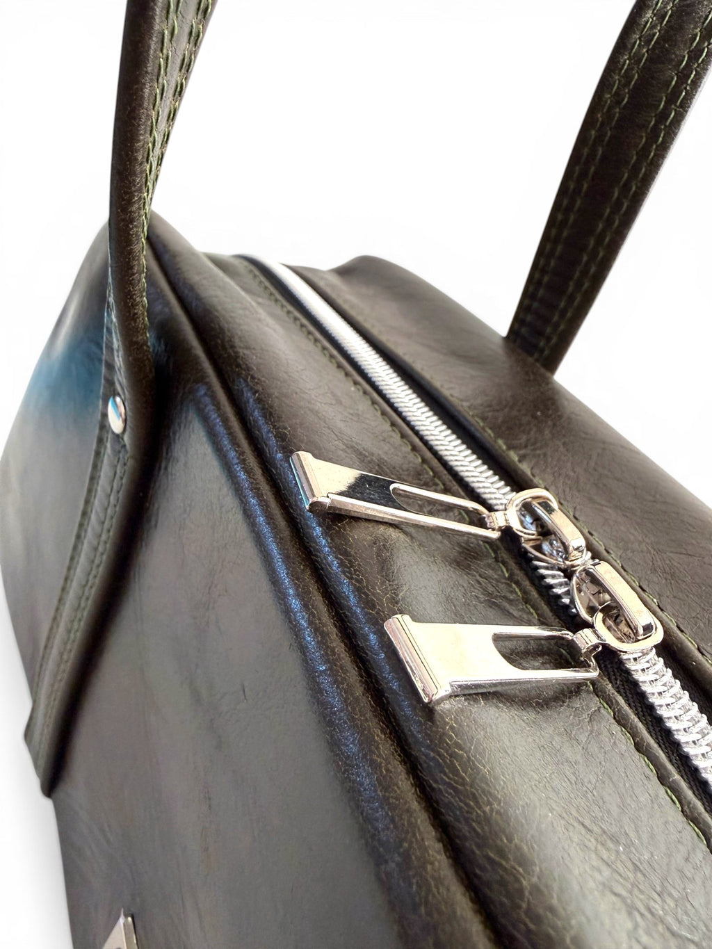 Close-up of a dark green leather handbag with silver zippers on a white background