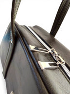 Close-up of a dark green leather handbag with silver zippers on a white background
