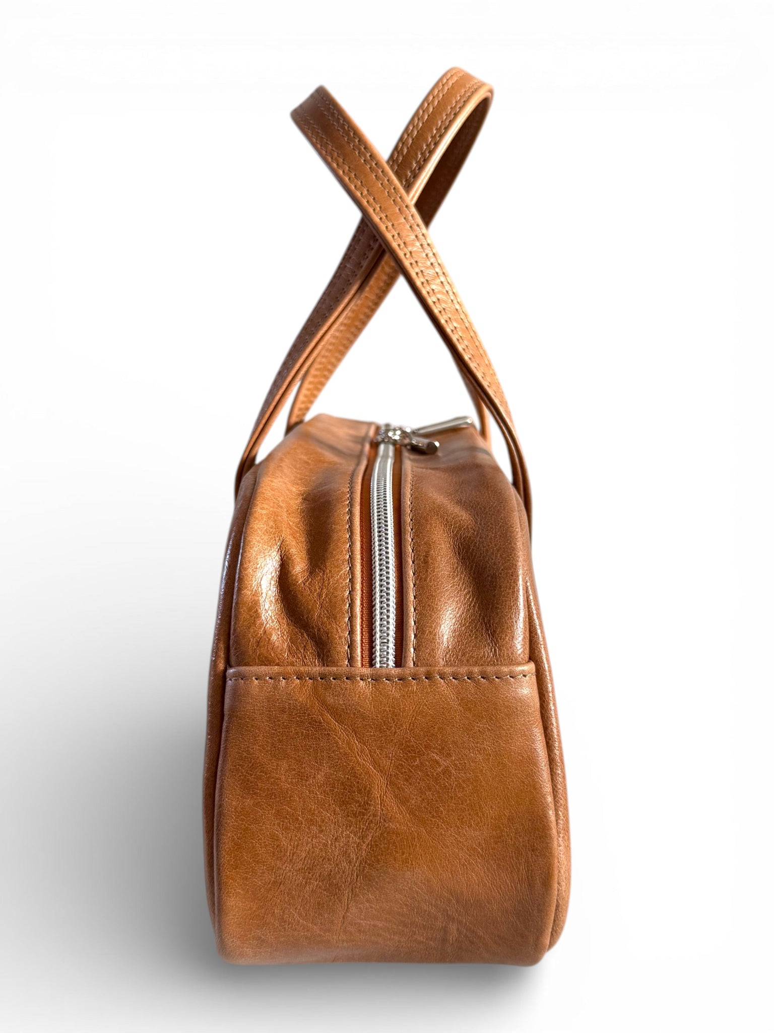 Side view of the tan coloured leather bowling style bag, showing the silver zipper closure