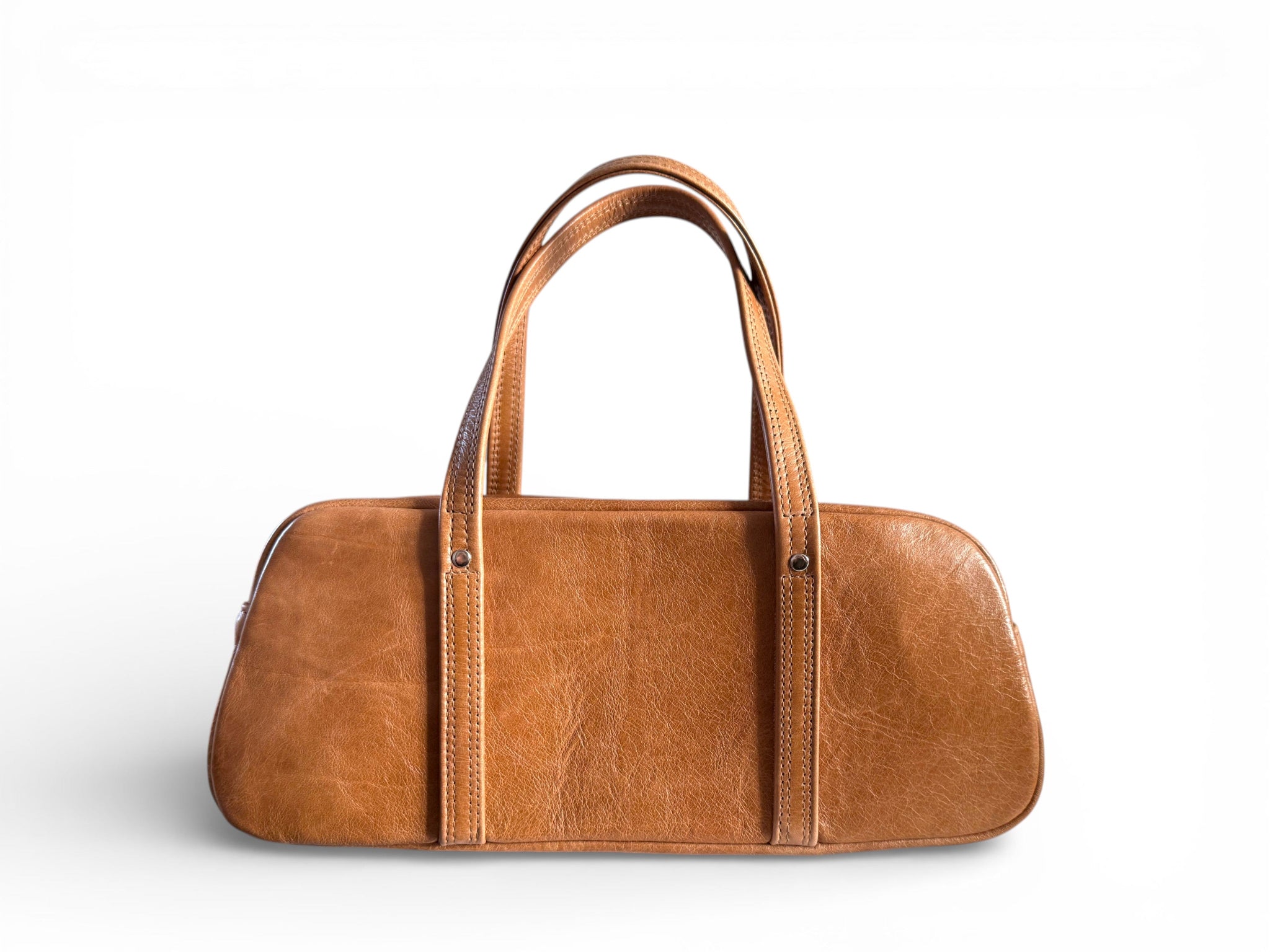 Rear view of a the Cassie baguette, bowler style bag. The bag is handcrafted using tan coloured rescued leather and is standing on a white background