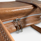 Close-up of a brown leather handbag with a silver zipper and zipper pulls on a white background.