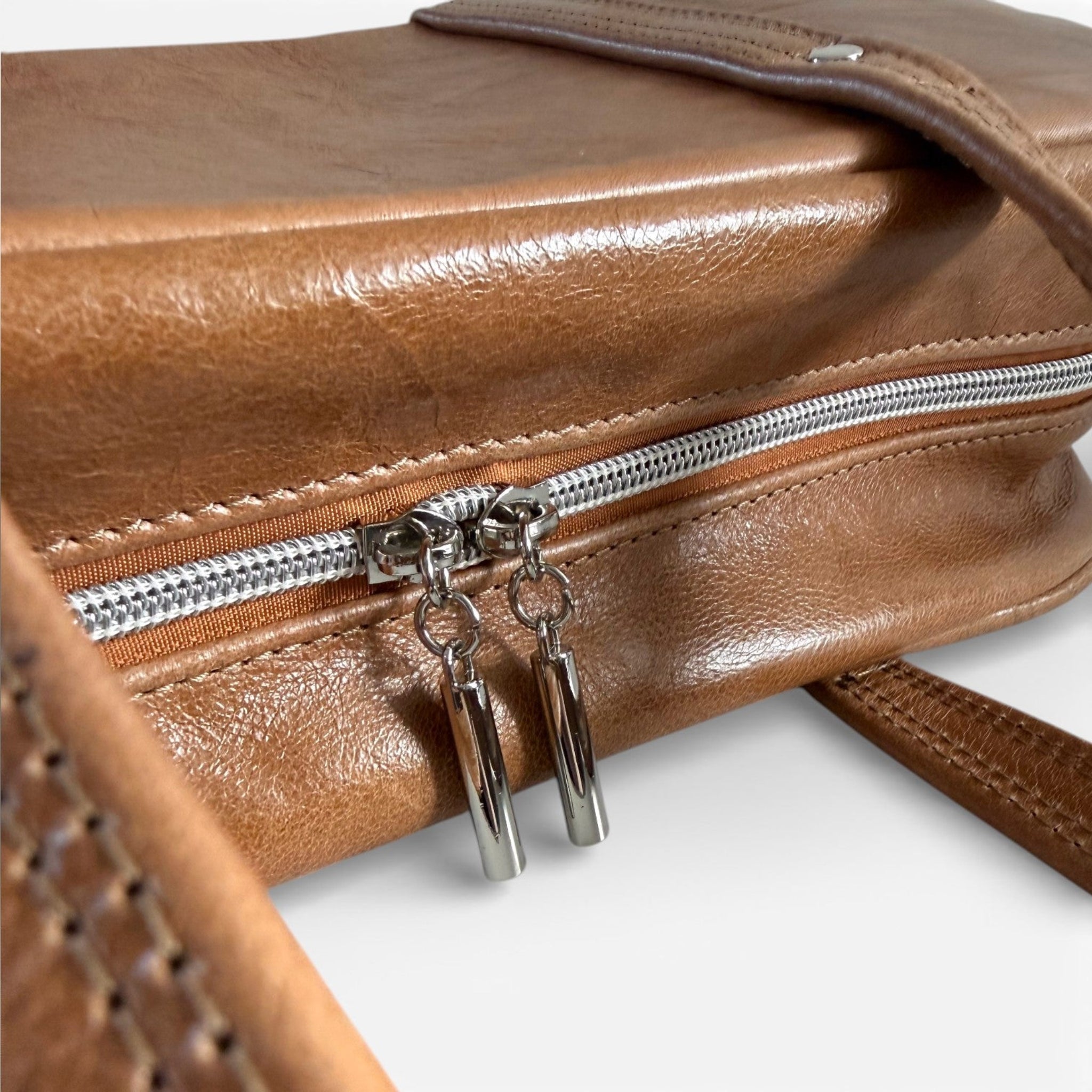 Close-up of a brown leather handbag with a silver zipper and zipper pulls on a white background.