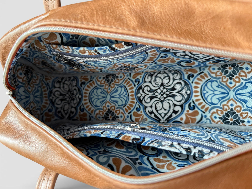 Tan brown leather bag with blue and white patterned interior lining on a light gray background