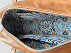 Tan brown leather bag with blue and white patterned interior lining on a light gray background