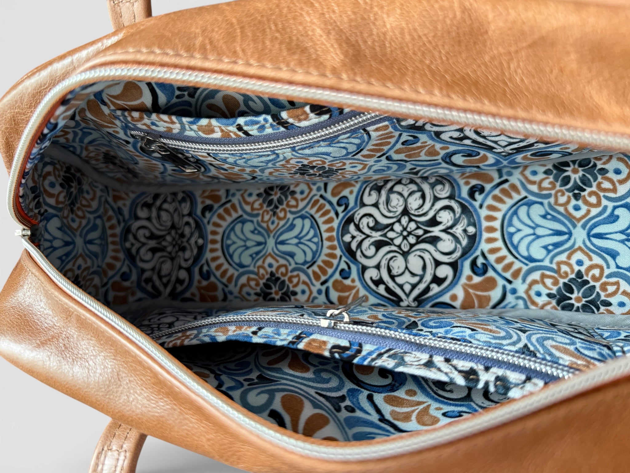Tan brown leather bag with blue and white patterned interior lining on a light gray background