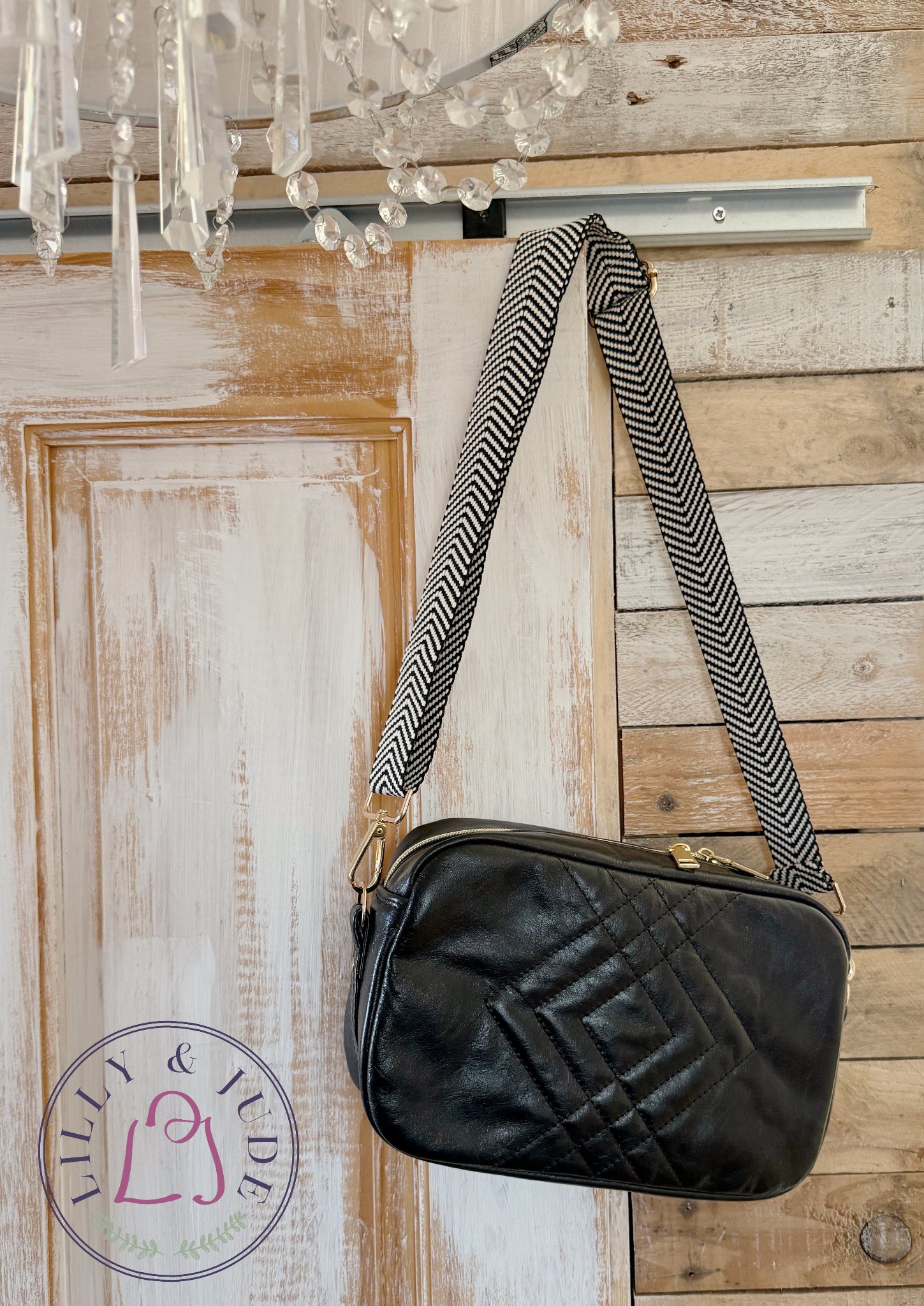 Handcrafted black, quilted leather crossbody handbag with an adjustable strap hanging on a wooden door.