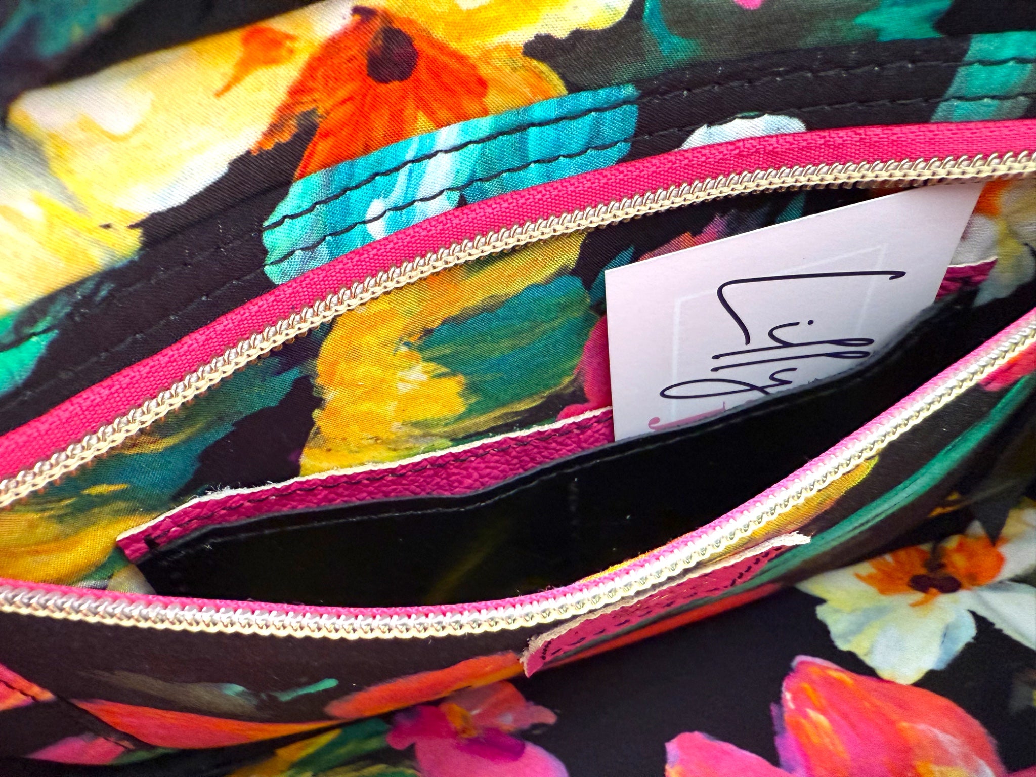 Closeup view of the interior of the Catalina bag. The image shows the lining fabric and the open slip/zip pocket, which contains a hidden integrated purse. Colorful floral-patterned bag with a visible brand tag.