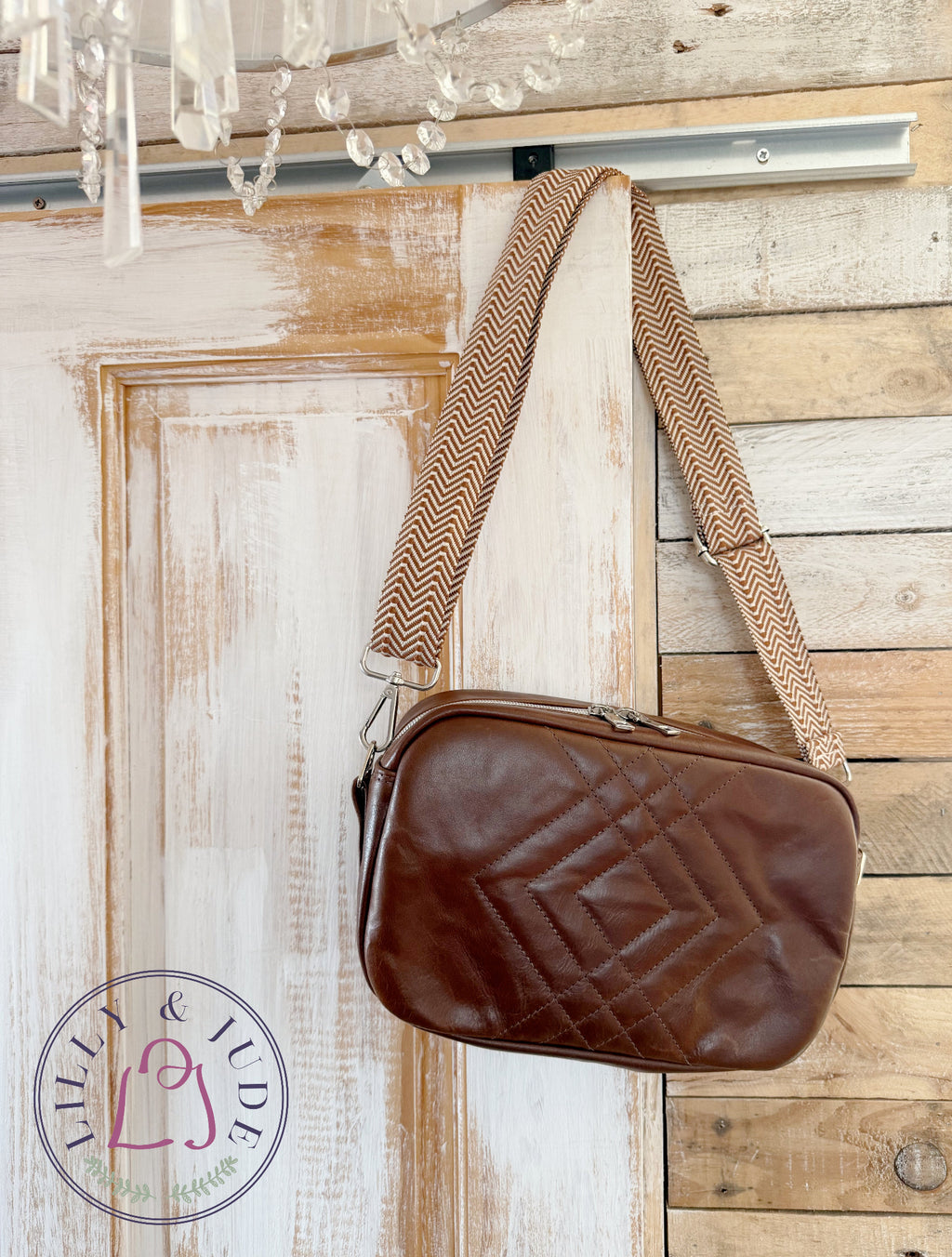 Catalina crossbody bag, handcrafted using rescued, brown leather, with a geometric, quilted front, hanging on a wooden door.