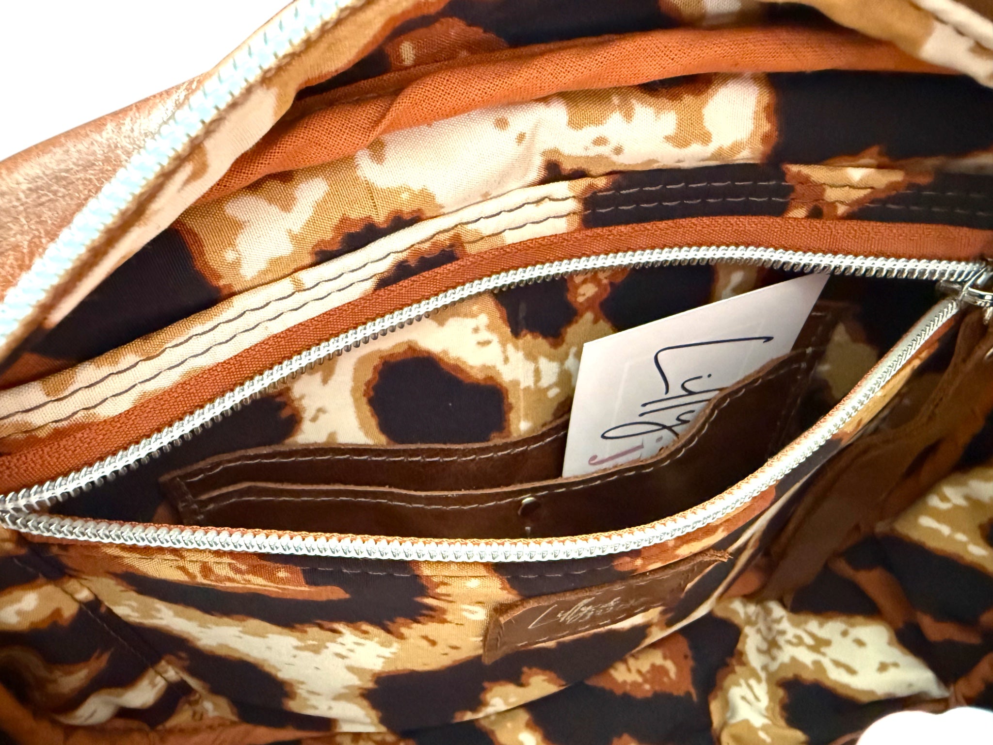 View of the interior of the brown leather Catalina bag, showing the leopard print lining and the slip/zip pocket open to reveal the integrated purse 