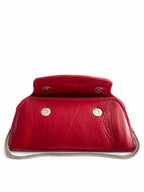 Red leather clutch bag with silver chain on white background. The front flap is slightly open to show the magnetic clasps