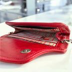Red leather wallet open to show the champagne and red patterned silk lining on a white surface.