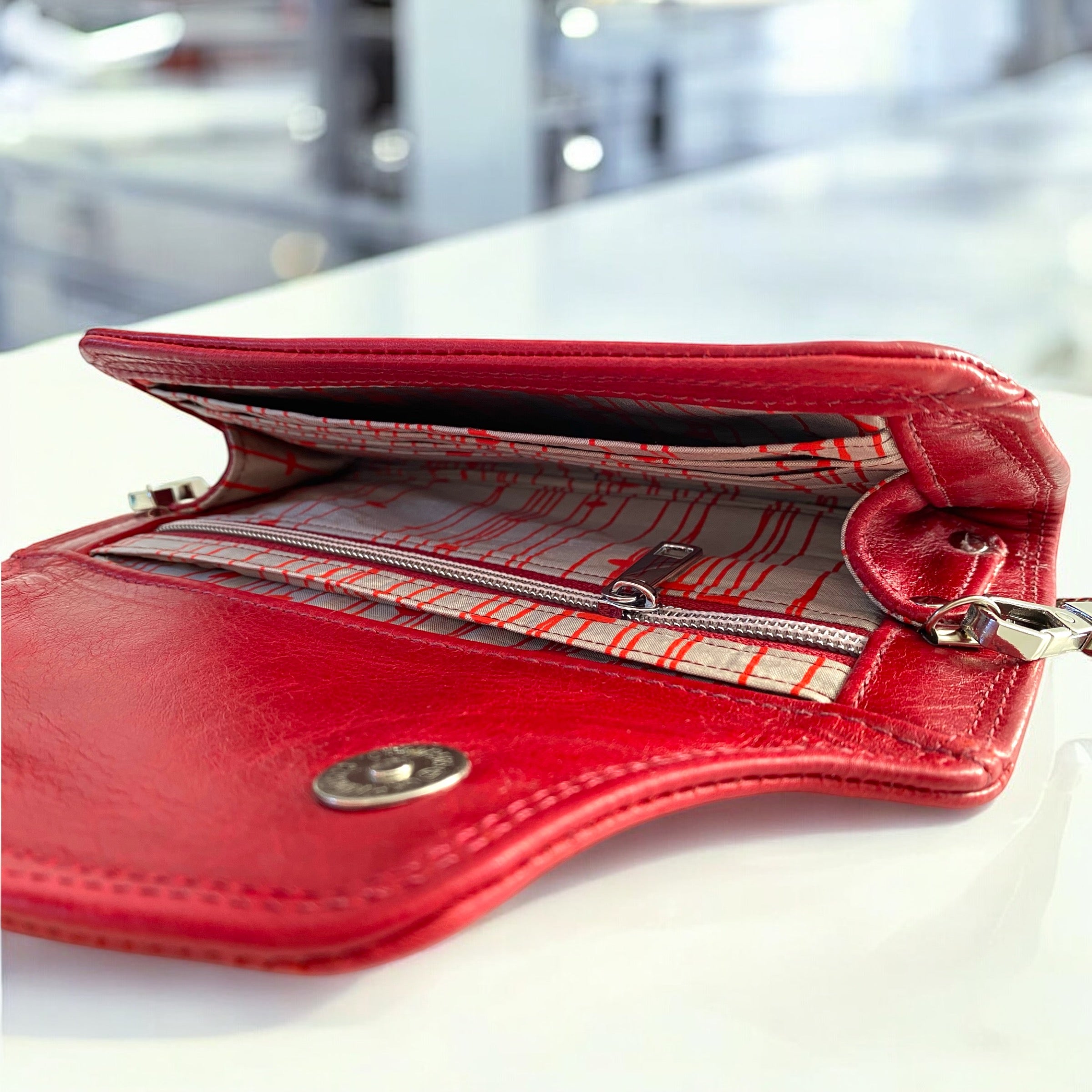 Red leather wallet open to show the champagne and red patterned silk lining on a white surface.