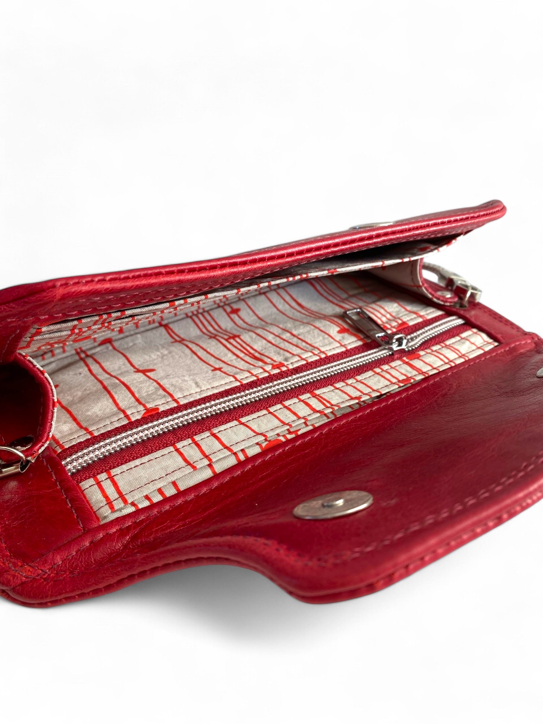 Red leather clutch bag open to show the interior zipper pocket and card slots, and champagne coloured silk lining on a white background