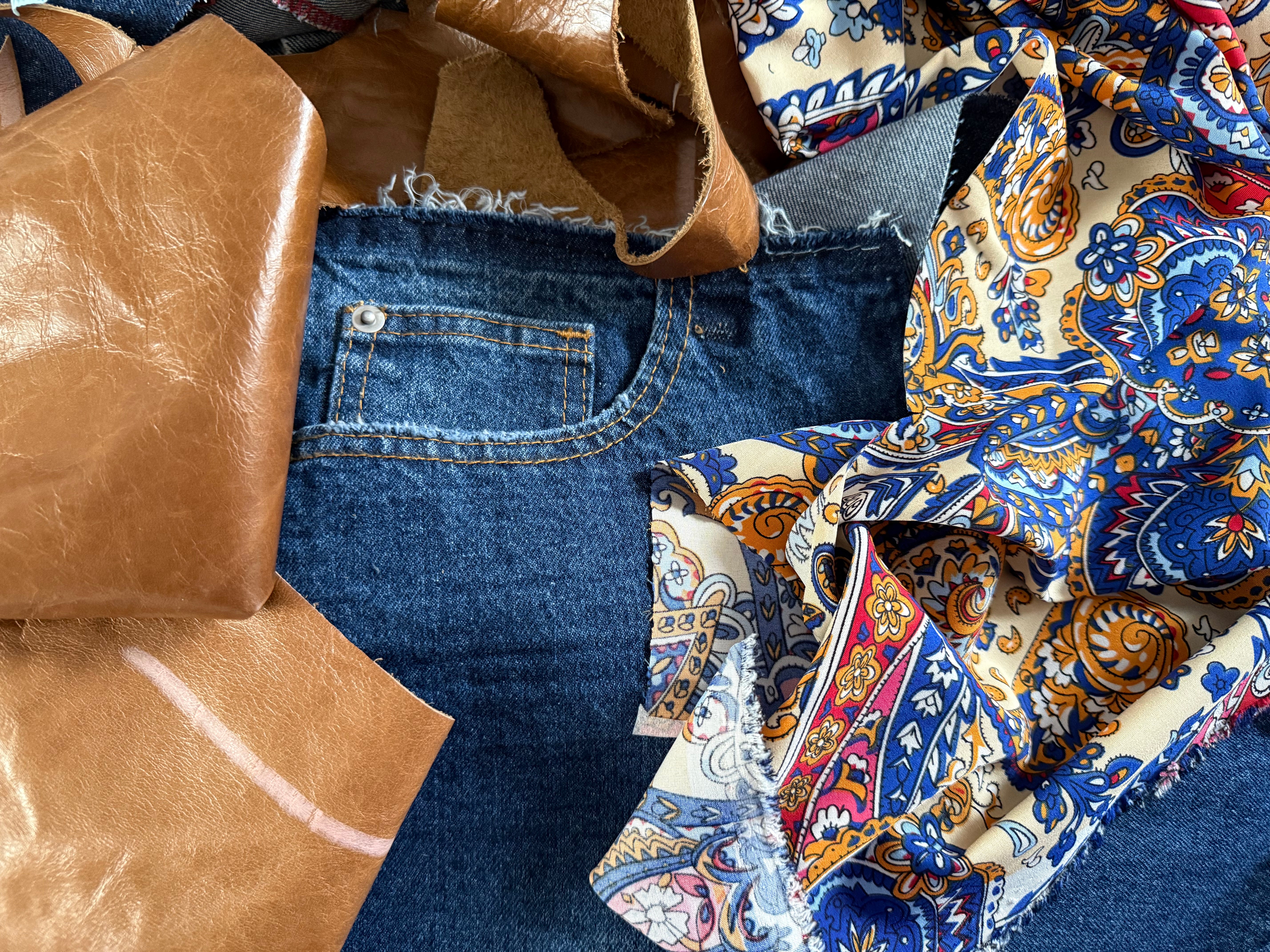 Blue jeans with scraps of brown leather and patterned fabric on a blue background