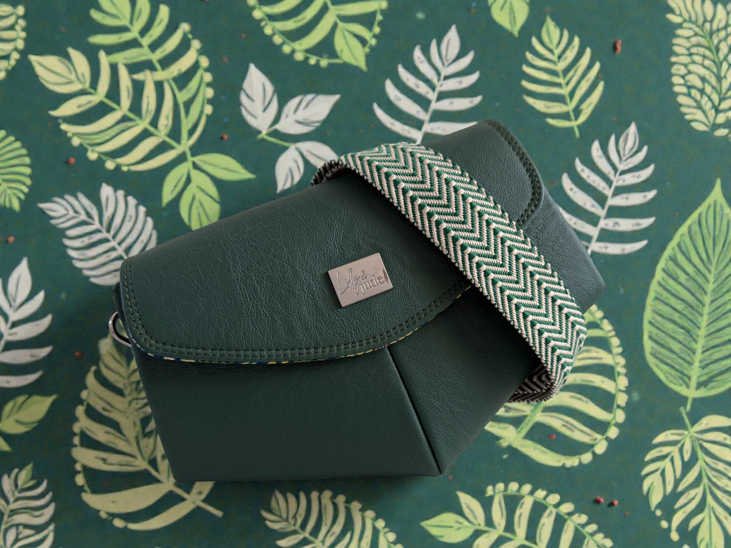 Green leather Skye clutch and crossbody bag, with a matching chevron patterned strap wrapped across the front of the bag. The bag is lying green, leaf patterned paper