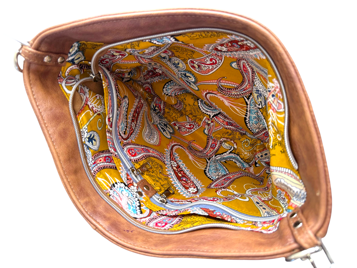 A brown leather handbag shown from a top-down view, highlighting its interior. The inside lining features a vibrant yellow background with a detailed paisley pattern in red, blue, and white.