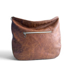 View of the back of a brown textured leather shoulder bag with a horizontal silver zipper pocket, shown against a plain white background.
