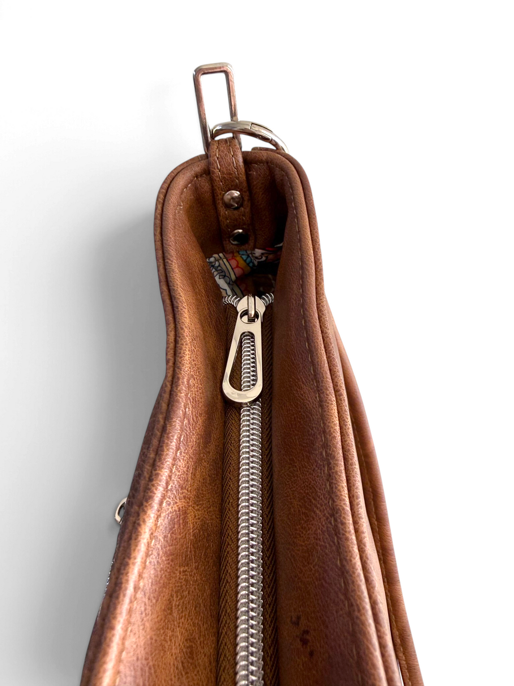 Close-up of a brown leather zippered handbag with a silver metal zipper pull and hardware, shown against a plain white background.