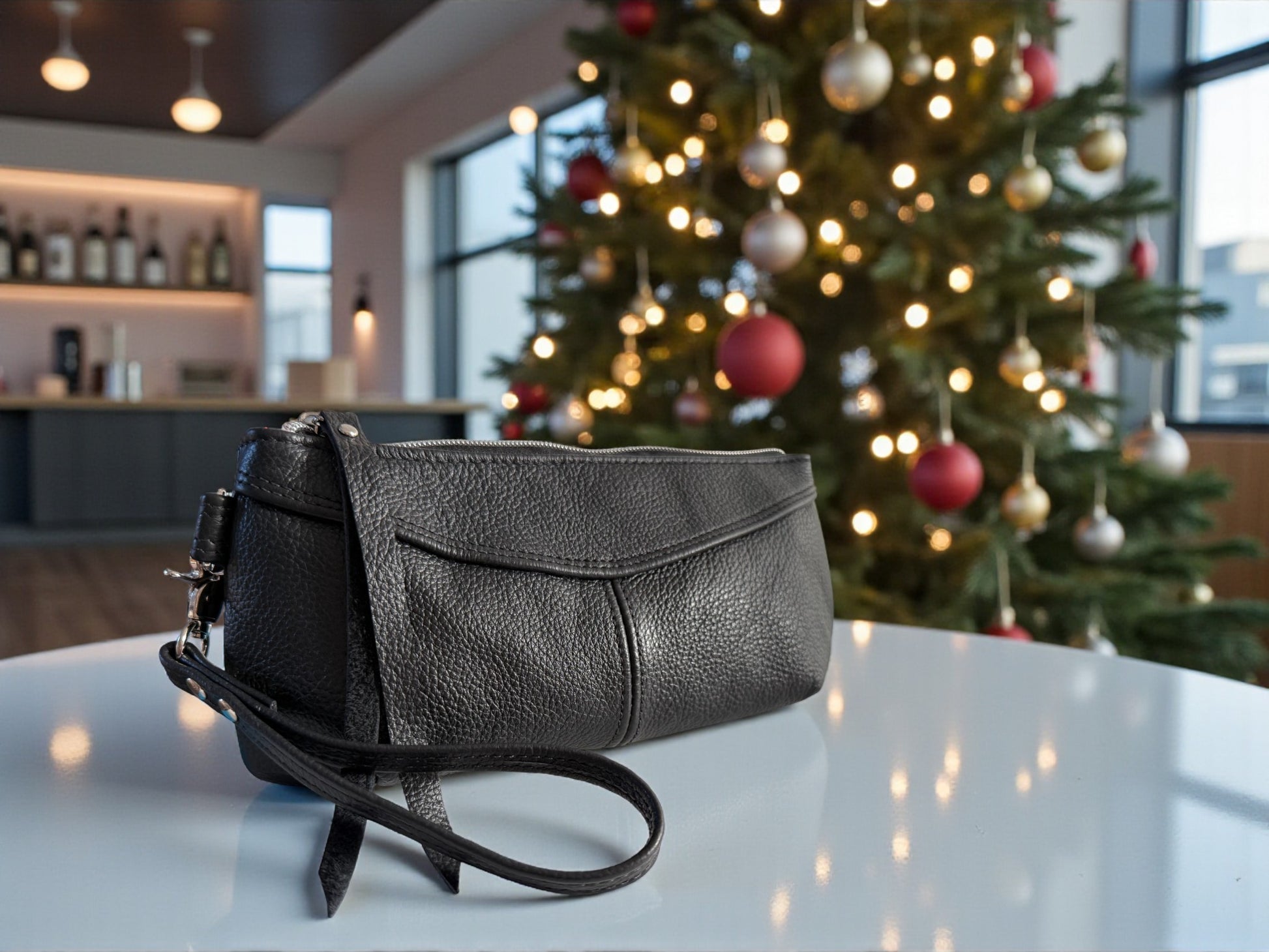 Black leather wristlet bag on a table with a decorated Christmas tree in the background. 