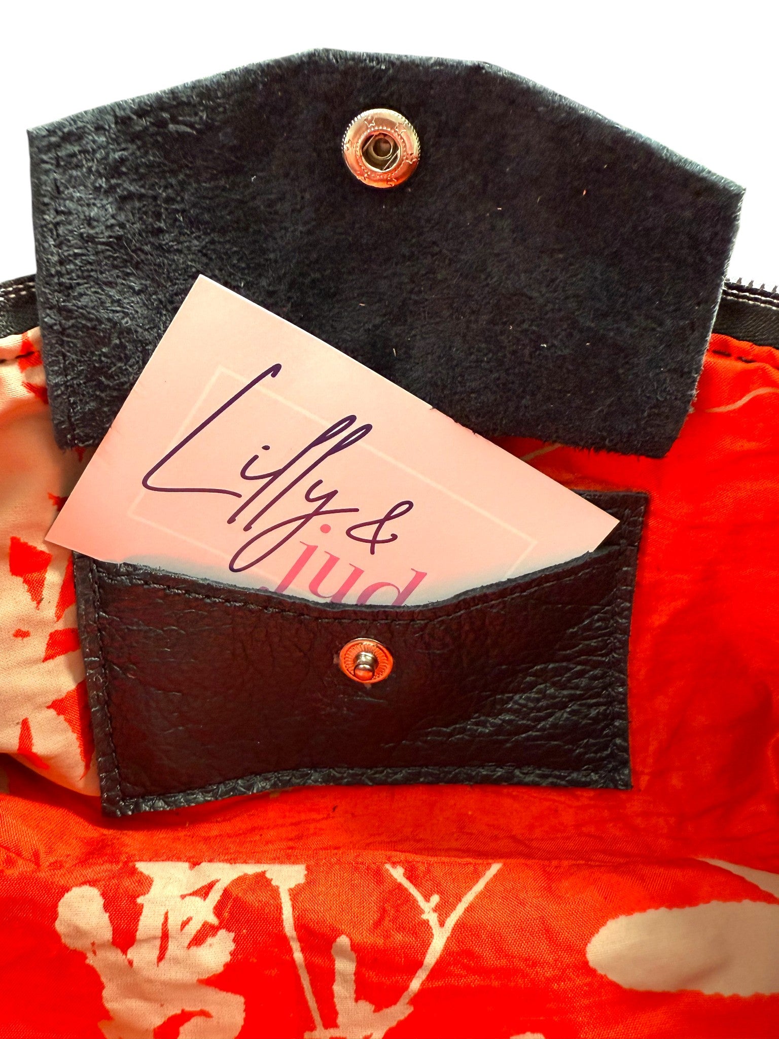 Interior view of the Ella Wristlet Clutch Bag, showing the red silk lining and the open integrated purse, with  a Lilly & Jude business card, showing where your bank card can be stored