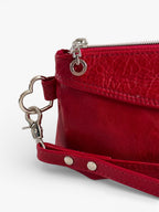 Red leather clutch bag with wrist strap and heart-shaped keychain on a white background