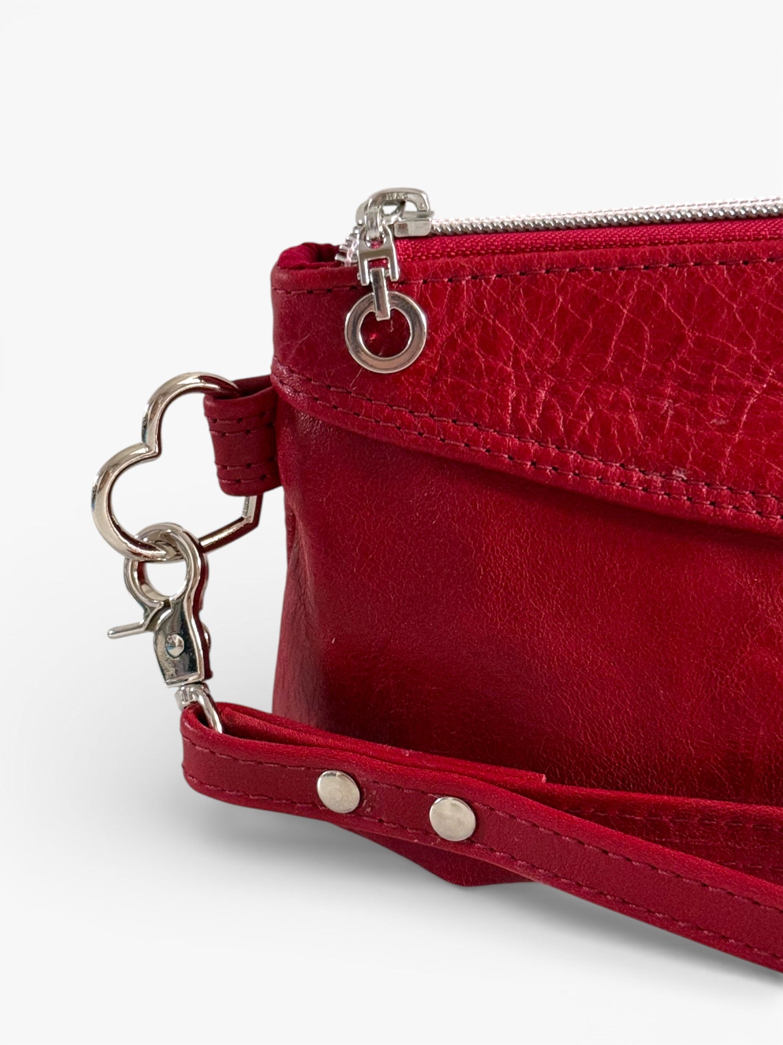 Red leather clutch bag with wrist strap and heart-shaped keychain on a white background