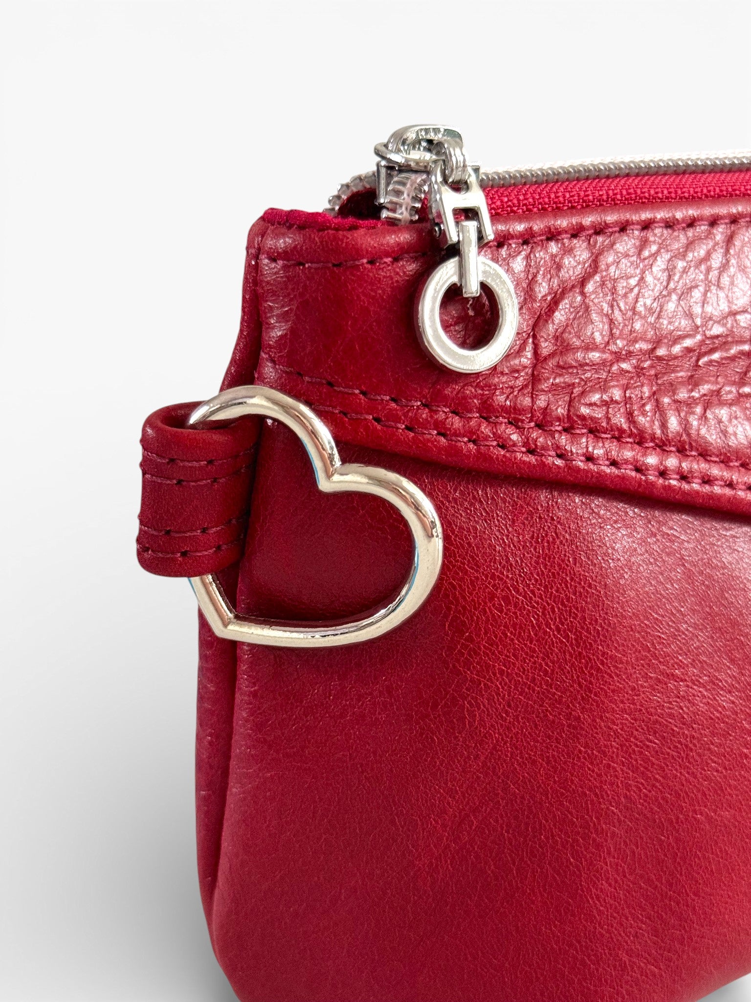 Red leather handbag with a heart-shaped clasp on a white background