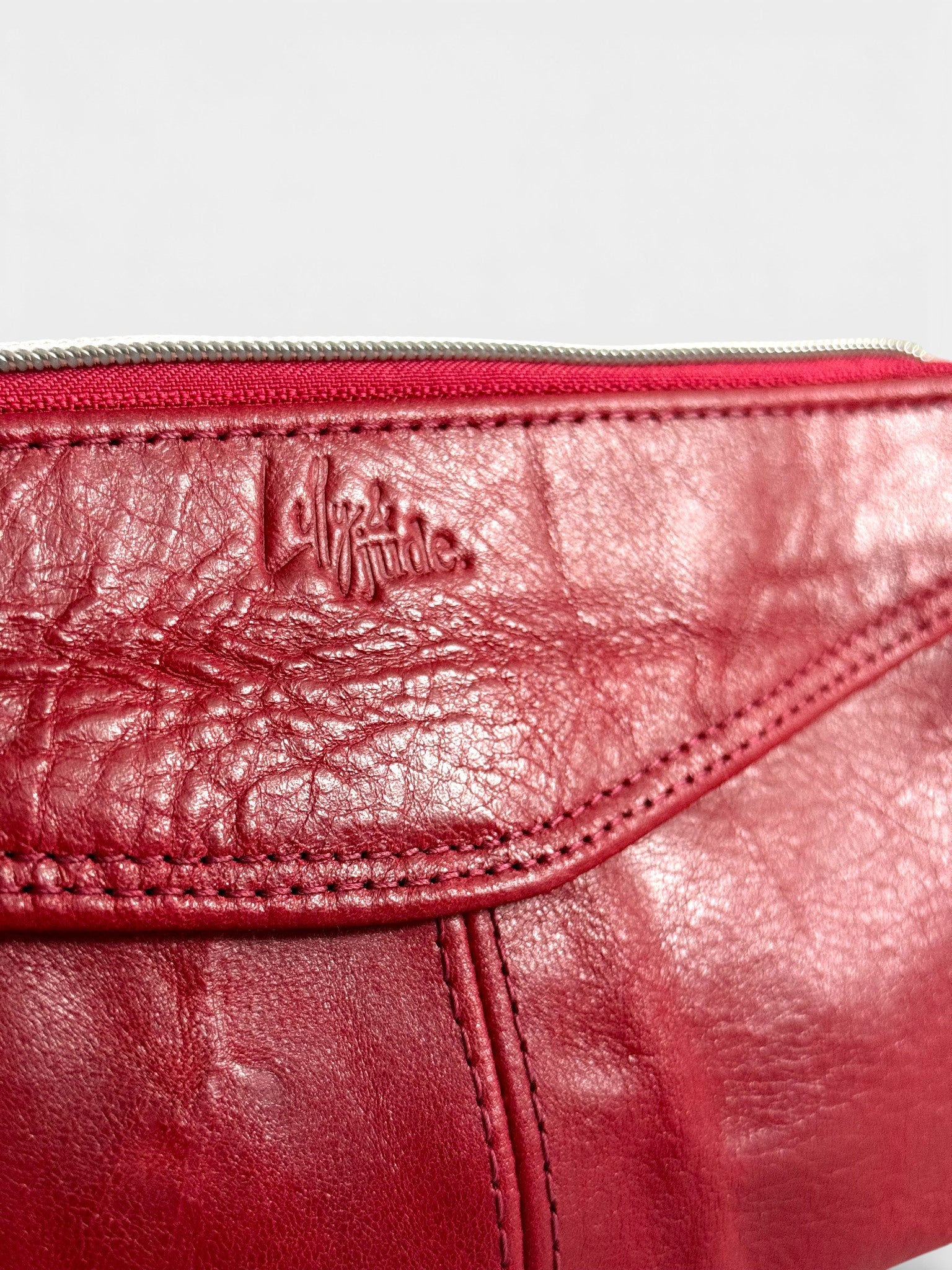 Close-up of a red leather bag with a Lilly & Jude logo on a light gray background