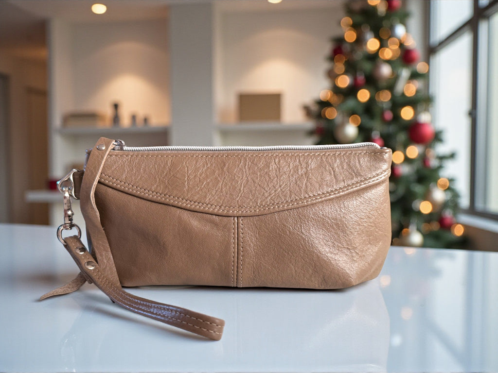 Handcrafted taupe leather clutch bag on a surface with a blurred Christmas tree in the background. Exclusive design by Lilly & Jude