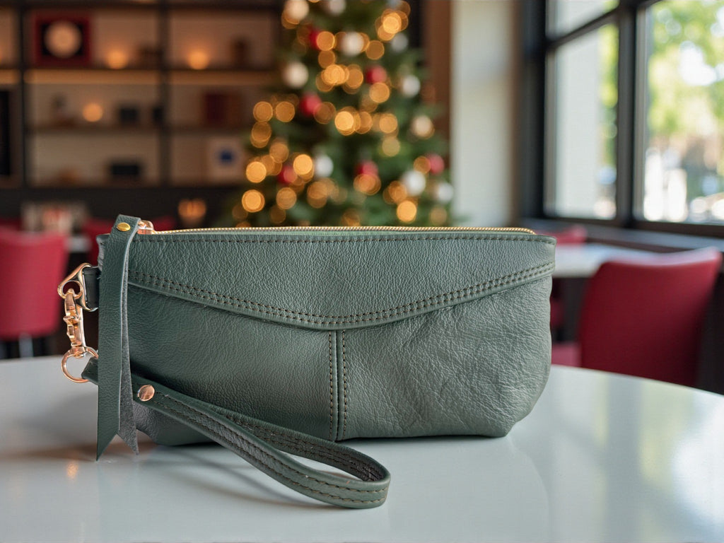 Green leather clutch bag on a table with a blurred Christmas tree in the background