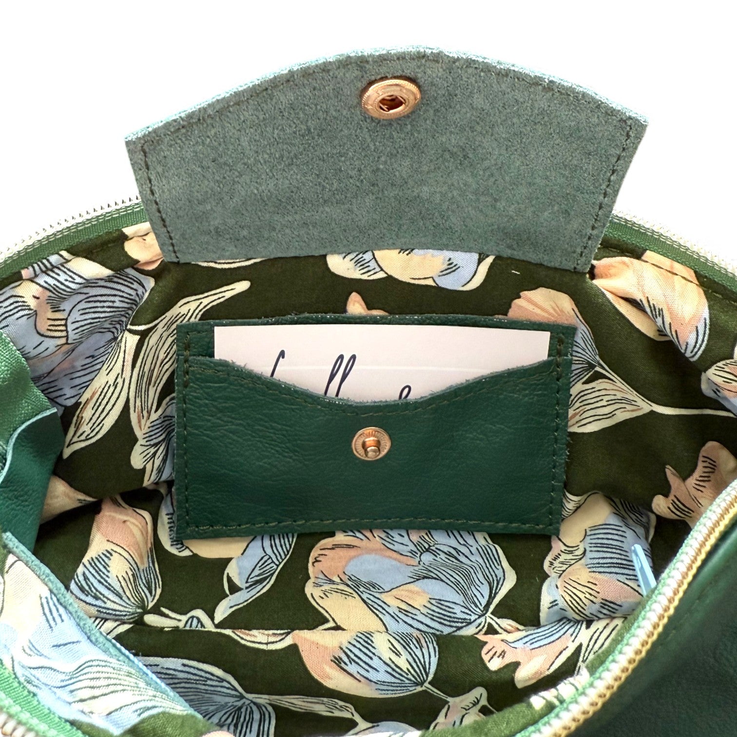 Interior view of the green Ella wristlet clutch bag, showing the green and blue floral patterned lining and leather integrated purse, with the flap open to show the card slot. Exclusive to Lilly & Jude