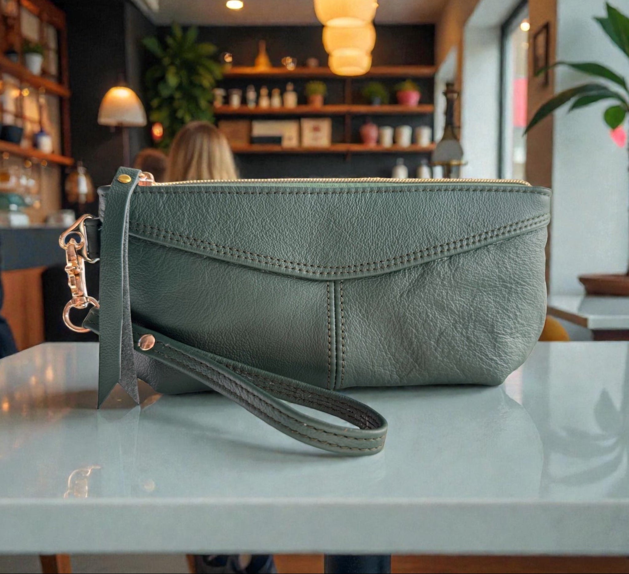 Green leather clutch on a table with a blurred cafe background