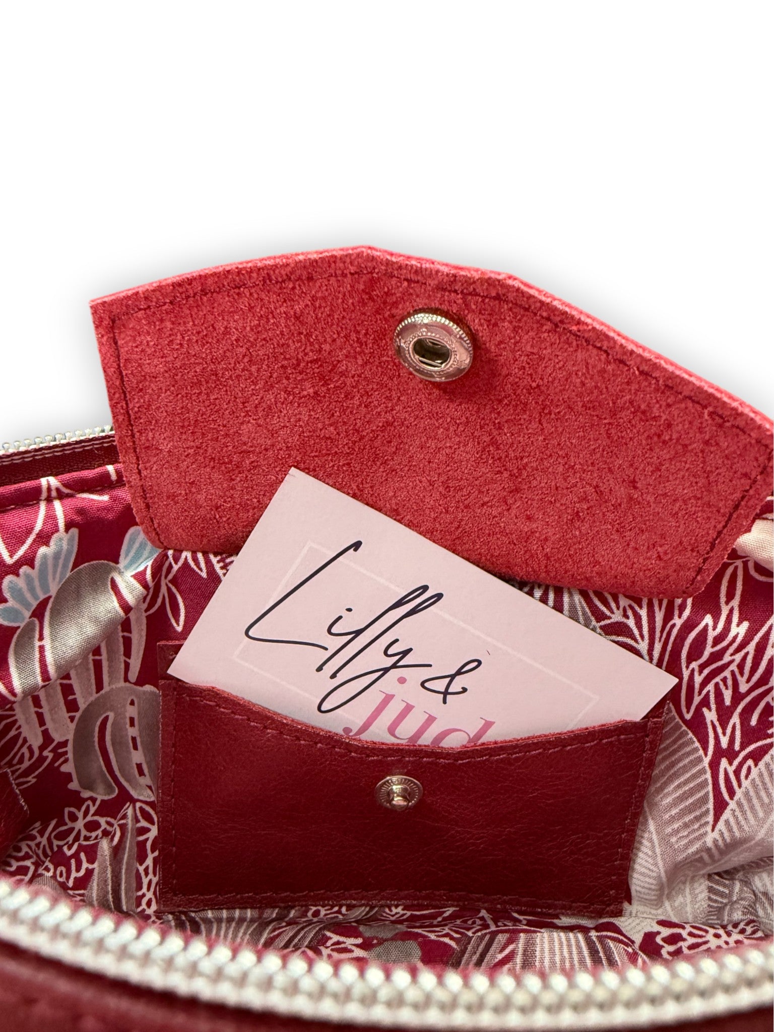 Interior view of the red pouch, showing the integrated purse open with a pink business card inside, featuring the brand 'Lilly & Juder'.